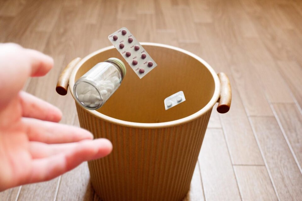 Hand dropping pills blister pack and medicine bottle into trash can for safe disposal, household waste cleanup service Acworth, GA