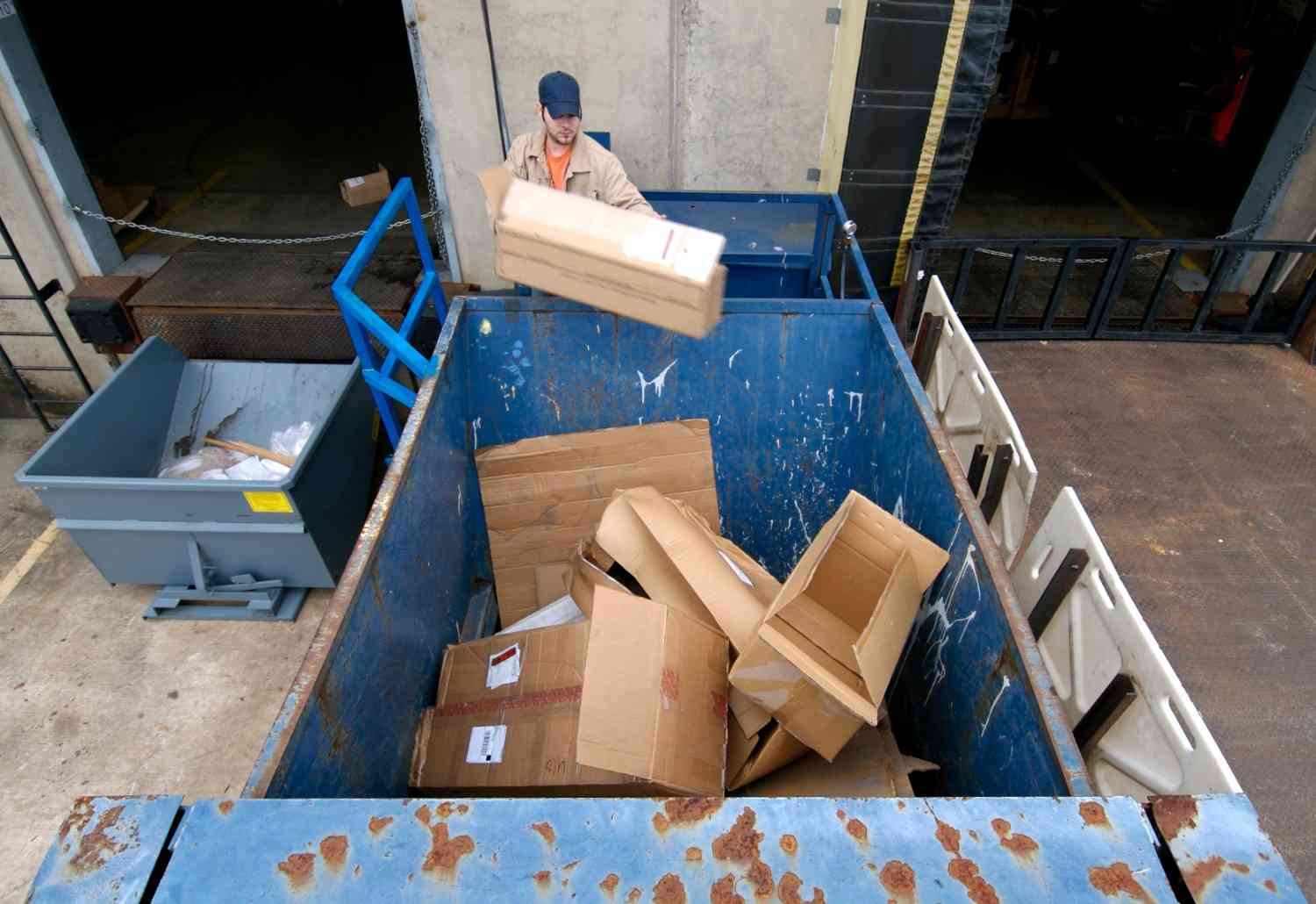 Worker loading cardboard into a dumpster rental container during a cleanup project in Acworth, GA